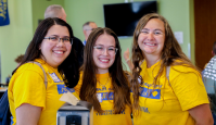 Three peer mentors smile for the camera in the cafeteria during first year orientation