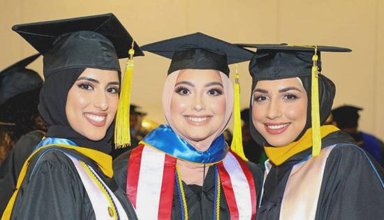 three graduates smile for the camera in their graduation caps and gowns