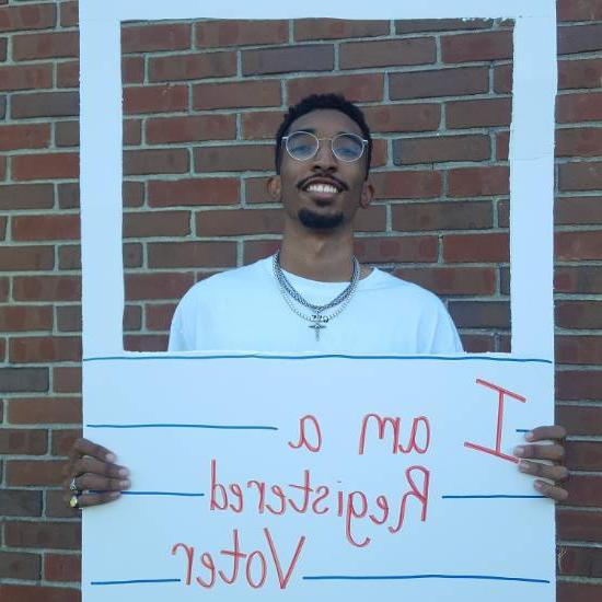 Man holding up sign with cutout framing his profile that reads "I'm a registered voter"